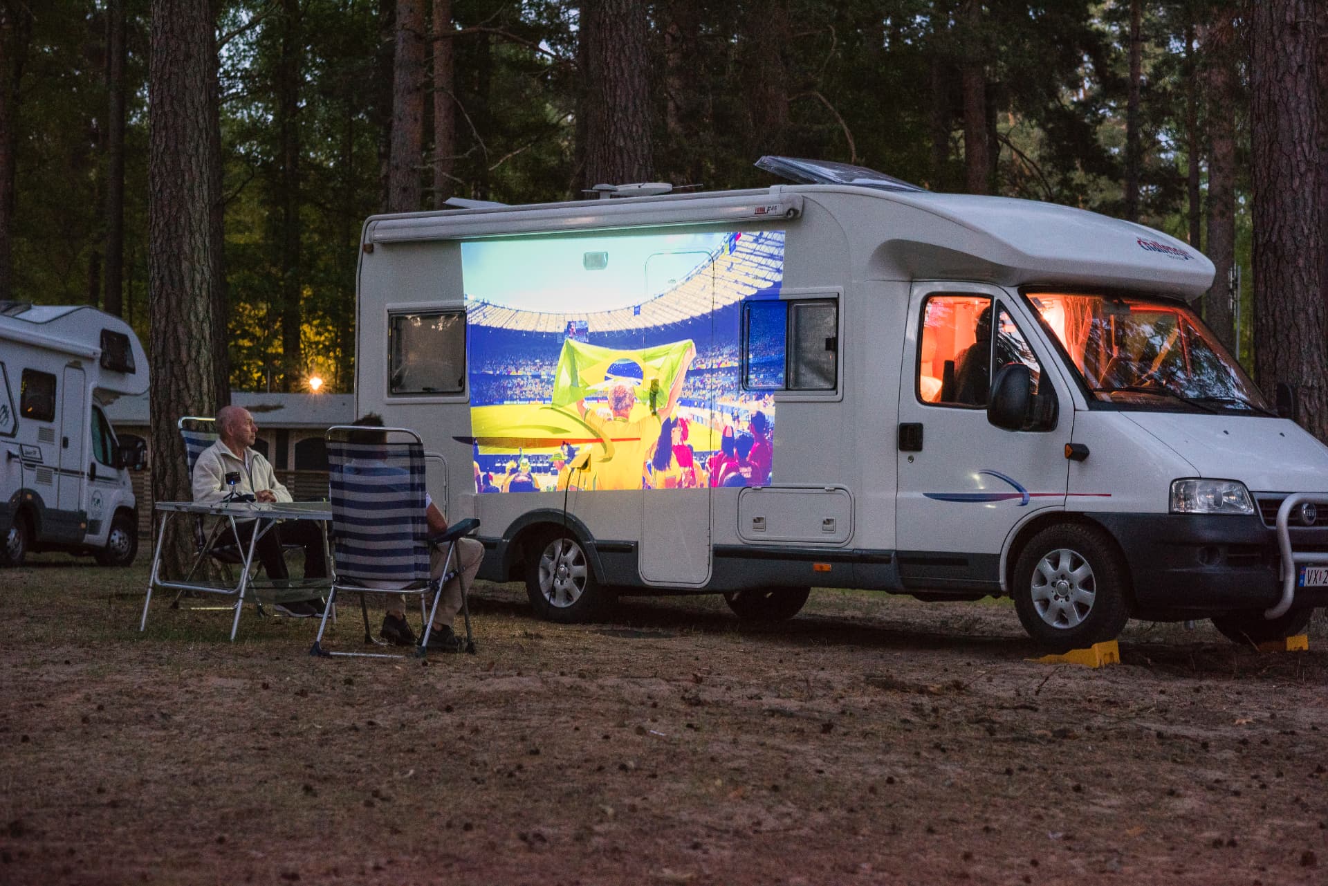 Husbil på camping i skogen med fotboll projicerad på sidan av bilen