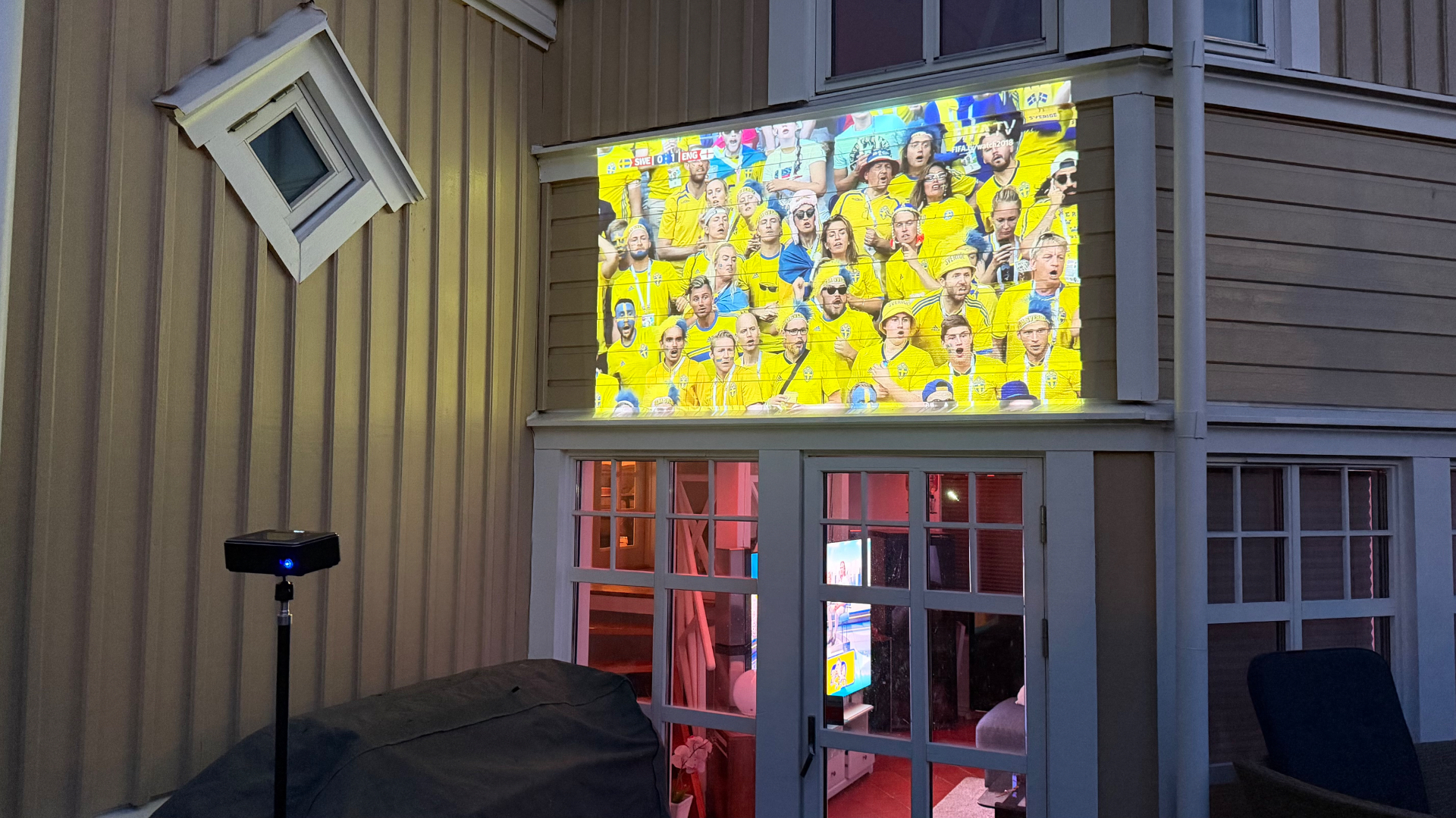 PICZO Nova Ultra S på stativ projicerar en fotbollsmatch på en villafasad i skymning
